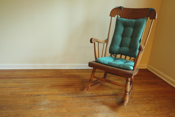 Old rocking chair in the corner of a room with old hardwood flooring. 