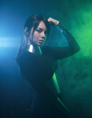 Fototapeta na wymiar futuristic fashion model wearing black and silver clothes and standing in the colorful blue and green smoke
