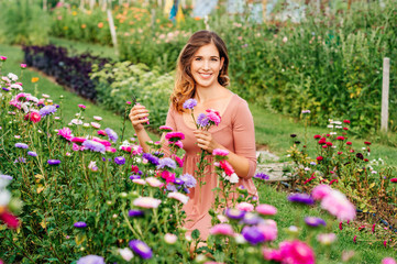 Pretty young woman working in autumn garden, girl taking care of colorful chrysanthemum, gardener enjoying warm and sunny day