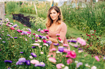 Pretty young woman working in autumn garden, girl taking care of colorful chrysanthemum, gardener enjoying warm and sunny day