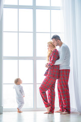Happy family standing near a huge modern plastic window. Mother, father and little son are dressed in plaid pajamas