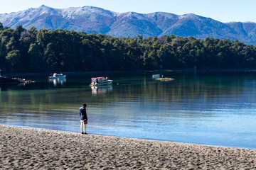 Paisaje de un lago con botes y una persona sobre la arena