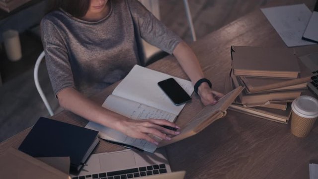Top view of young woman student in casual clothes working with book at table and taking notes. Concept of education and research. Left to right pan real time shot