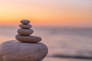 Obraz na płótnie Canvas Perfect balance of stack of pebbles at seaside towards sunset. Concept of balance, harmony and meditation. Helping or supporting someone for growing or going higher up.