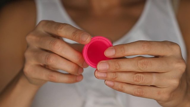 Woman holding a new pink menstrual cup in hands and showing how to make punch down fold to insert it
