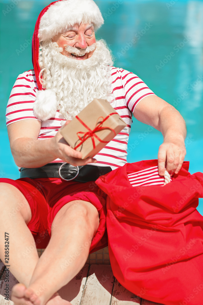 Wall mural Santa Claus with gifts near swimming pool at resort