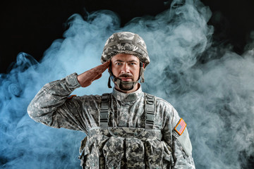 Saluting soldier on dark background with smoke