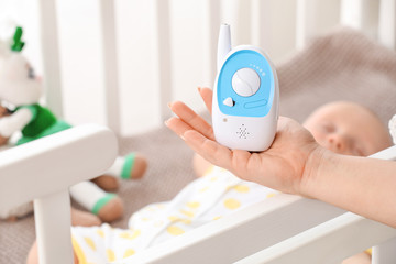 Fototapeta na wymiar Female hand with modern baby monitor and little sleeping child on background
