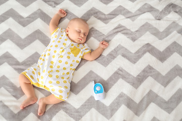 Modern baby monitor and sleeping infant on bed