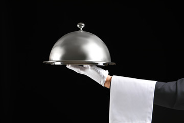 Hand of waiter with tray and cloche on dark background