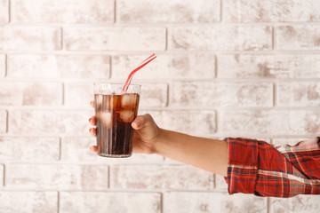 Female hand with glass of cold cola against brick wall