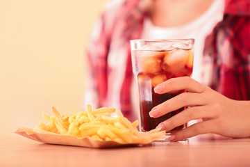 Woman with glass of cold cola and french fries at table