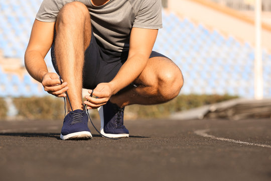 Handsome sporty man tying shoelaces at the stadium