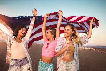 Young friends carrying american flag on the beach