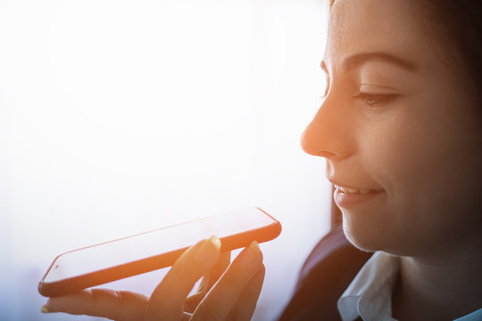 Young Smiling Business Woman Using Vocal Or Voice Activated Digital Assistant In Smartphone