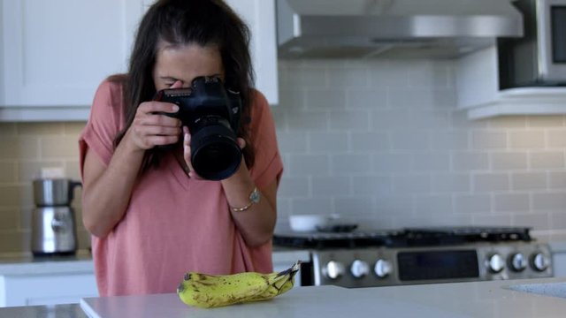 Female food photographer taking photo of bananas in kitchen - wide shot