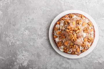 Homemade cake with milk cream, cocoa, almond, hazelnut on a gray concrete  background with orange textile. Top view, copy space.
