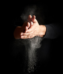 man claps his hands and scatters to the side a white substance on a black background