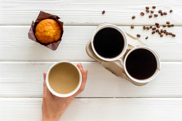 Coffee to take away in paper cups in hands, beans with muffin on white wooden table background top...