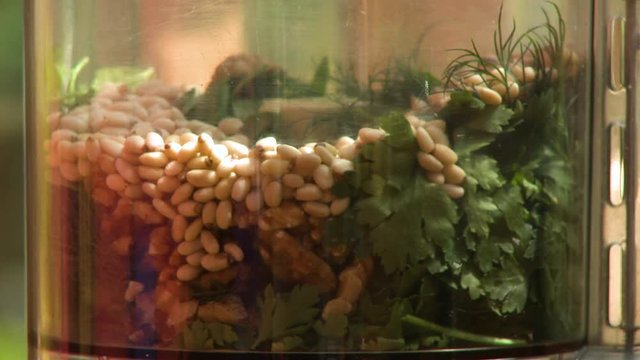 Steady, close up shot of beans being poured in a food processor containing green herbs.