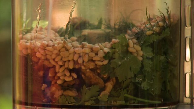 Steady, close up shot of liquid being poured onto leaves, beans and herbs in a food processor.
