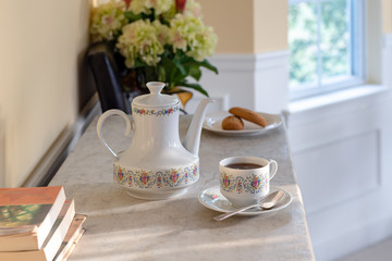 Antique White Porcelain Tea and Coffee Pot with Cup with Stacked Books in Foreground on a Late Afternoon in a Gold Dining Room