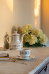 Tea Cup and Books on a Marble Table with White Teapot and Flowers in Late Afternoon Golden Light