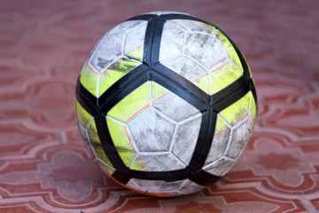 White leather soccer ball. On the ball there are abrasions obtained during football game. The ball is on the floor, lined with brown tiles with a geometric pattern.