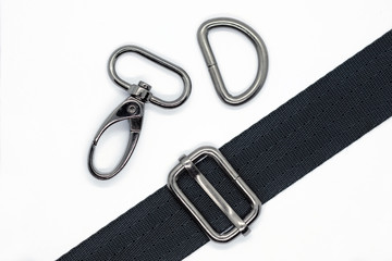 Sewing metal fittings for making bags and backpacks. Carabiner, half ring and length adjuster in dark nickel color on white background. Black tape for making different types of bags.