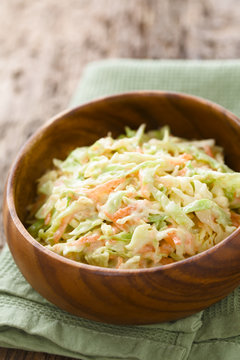 Coleslaw made of freshly shredded white cabbage and grated carrot with homemade mayonnaise-based salad dressing in wooden bowl (Selective Focus, Focus one third into the salad)