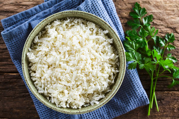 Freshly grated raw cauliflower rice in bowl with fresh parsley leaves on the side, photographed...
