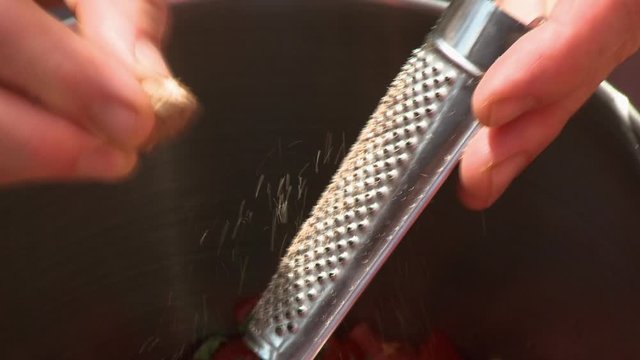 Handheld, close up shot of a person grating a garlic clove.