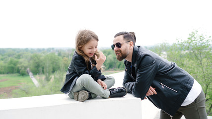 Fashionable stylish family for a walk. Charming schoolchild and her handsome young dad spend time together in the open air. Confidential conversation. Family look. Urban casual outfit. 