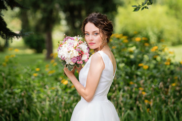 Beautiful bride in fashion wedding dress on natural background. The stunning young bride is incredibly happy. Wedding day. A beautiful bride portrait in the park.