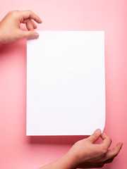 two hands holding blank page over pink background
