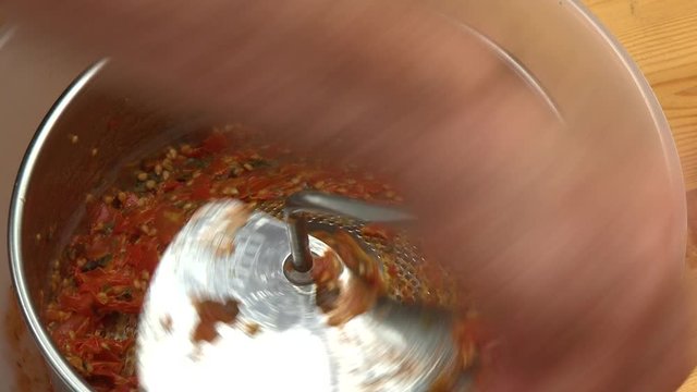 Handheld, aerial, close up shot of a hand cranking a blade as it strains salsa into a plastic bowl.