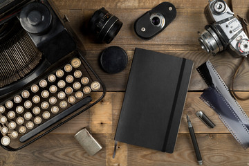 Vintage retro typewriter, analog film camera and notebook on brown wooden table background top view...