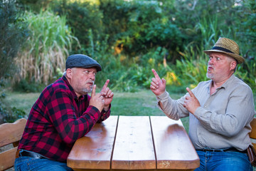 Two older men are sitting at a table discussing and arguing. Concept: quarrel and aggression