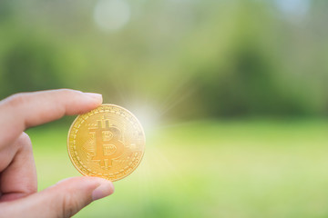 Hand hold a symbol of Bitcoins as cryptocurrency with nature background with copyspace that you can put text on.