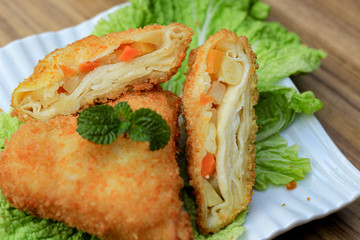 fried triangle risoles on a saucer with vegetables and chicken in it