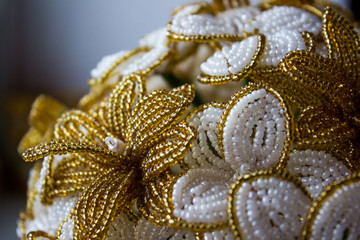 Beaded flowers are golden and white in daylight. Flowers from beads on a dark background.