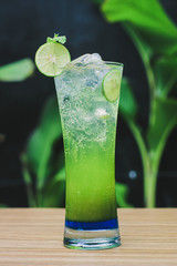 Cold lime mojito with melon syrup mixed in a glass beaker and shaken with soda displayed with chunks of lime and mint leaves