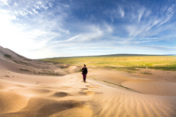 Fototapeta na wymiar Woman walking in the mongolian desert sand dunes. Young woman walking golden sand on a bright summer day, Mongolia holliday vacation concept.