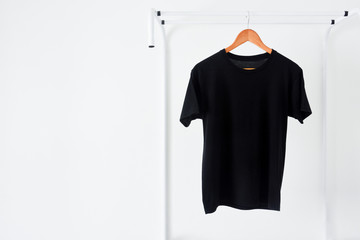 close up of black color t-shirt hanging on wooden cloth hanger on clothing rack over white background, copy space