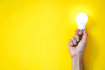 man's hand holding LED light bulb over yellow  color background with copy space, flat lay, concept...
