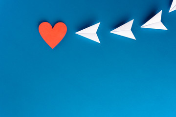 Focus, assertiveness, work yourself concept. Paper heart shape with airplane on blue background