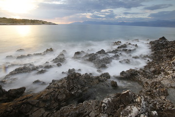 Sunset on a rocky Corfu beach with smooth waves