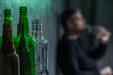 Close-up on empty bottles and blurred person drinking alcohol in the background