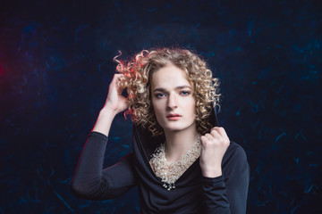 Handsome androgynous young man in the image of a woman passionately posing against a dark background, putting a hood over her face.