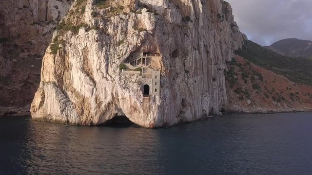 Drone shot of Porto Flavia an abandoned mineral storage pier in the coast of Sardinia in Italy.The shot is moving towards the cliff where the ornate entrance of the storage is placed.